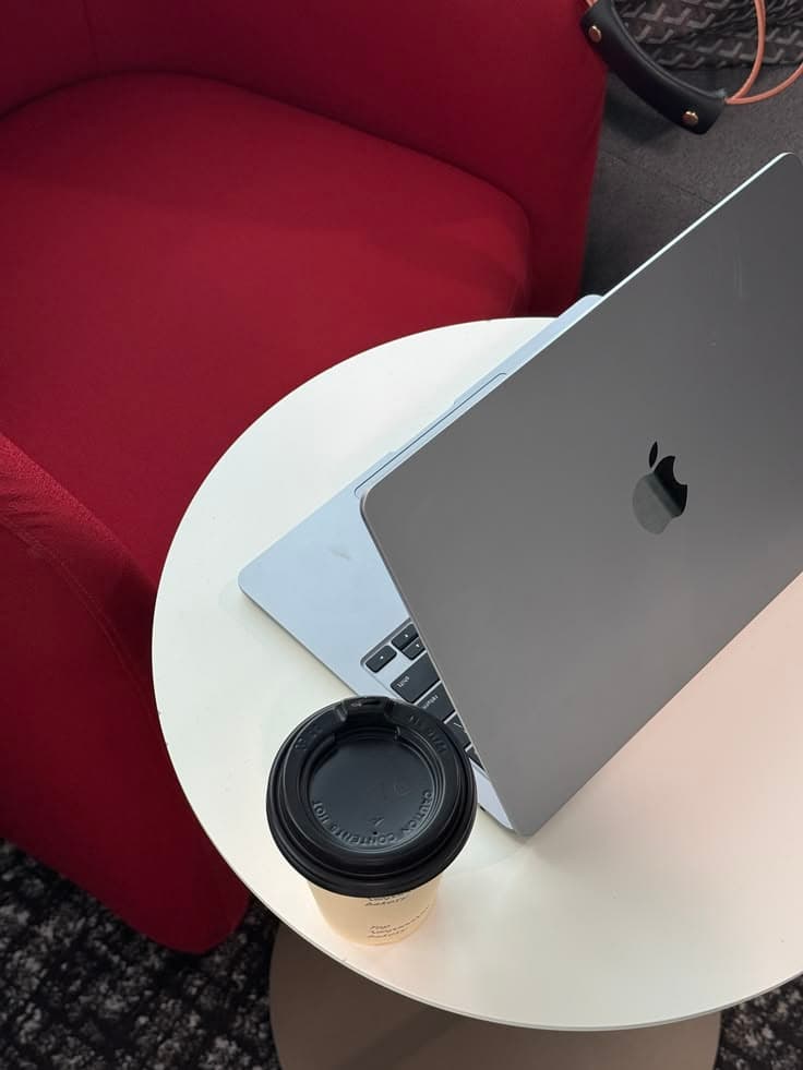 Silver laptop and a coffee cup on a white table beside a red chair.