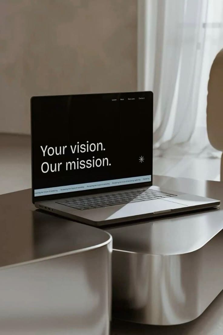 Laptop on a metallic table displaying the text "Your vision. Our mission." on the screen.